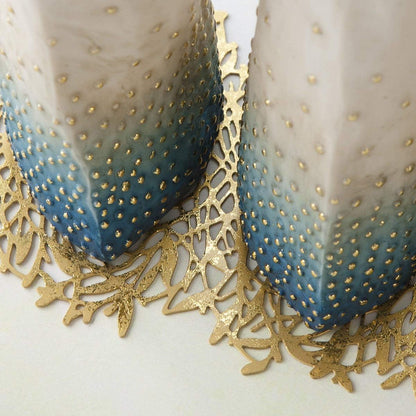 Two decorative candles with gold polka dots and a gold lace doily on a white background